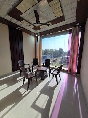 A spacious room with a ceiling fan, large windows with curtains, and a view of a landscape. - Hotel Siddhi Palace (Ayodhya)