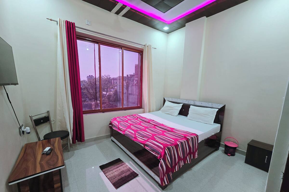 A bedroom with a bed, a desk, a chair, a window with curtains, and a ceiling with LED lighting.