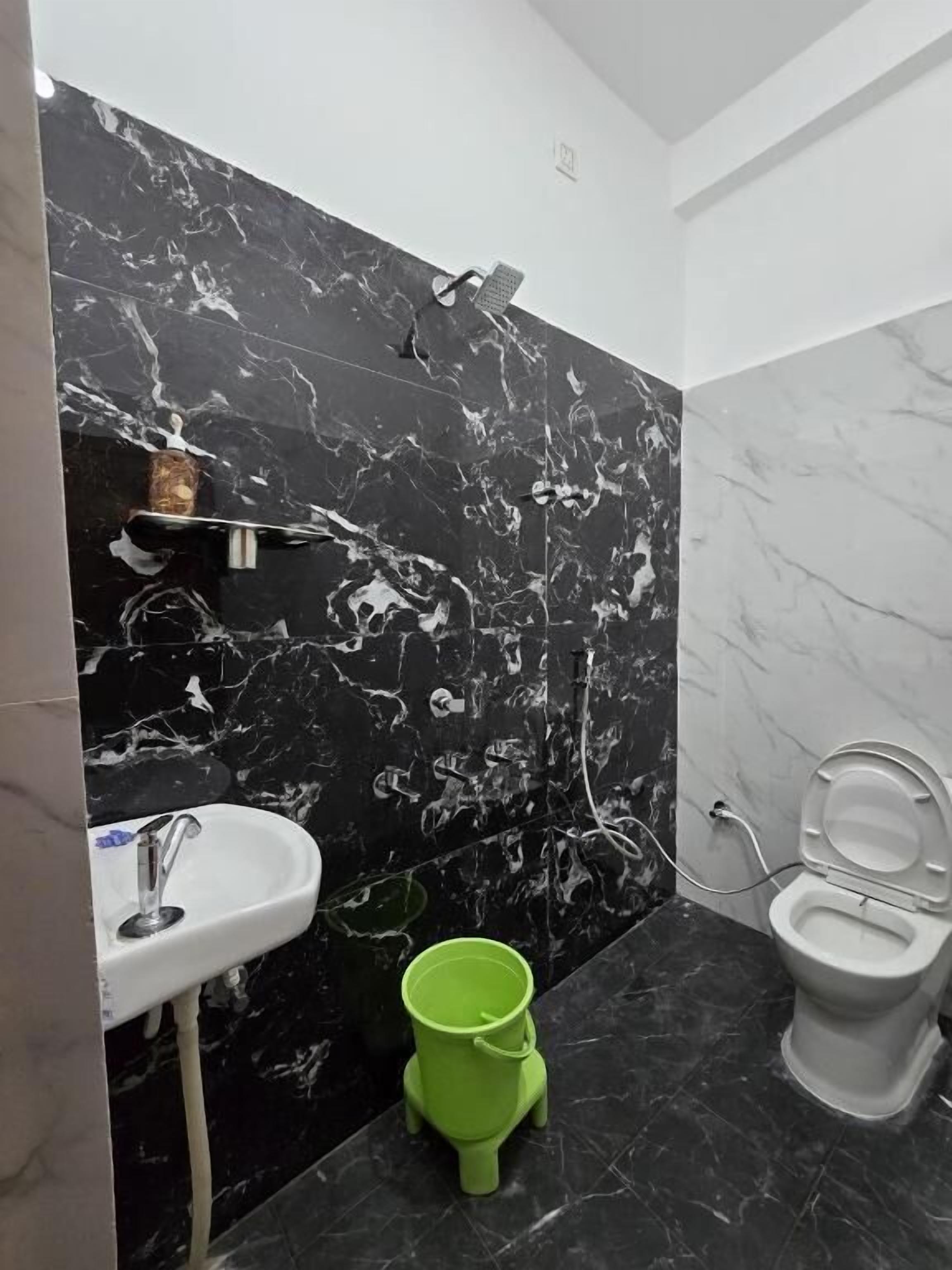 A bathroom with a black marble wall, a white sink, a green bucket, and a toilet.