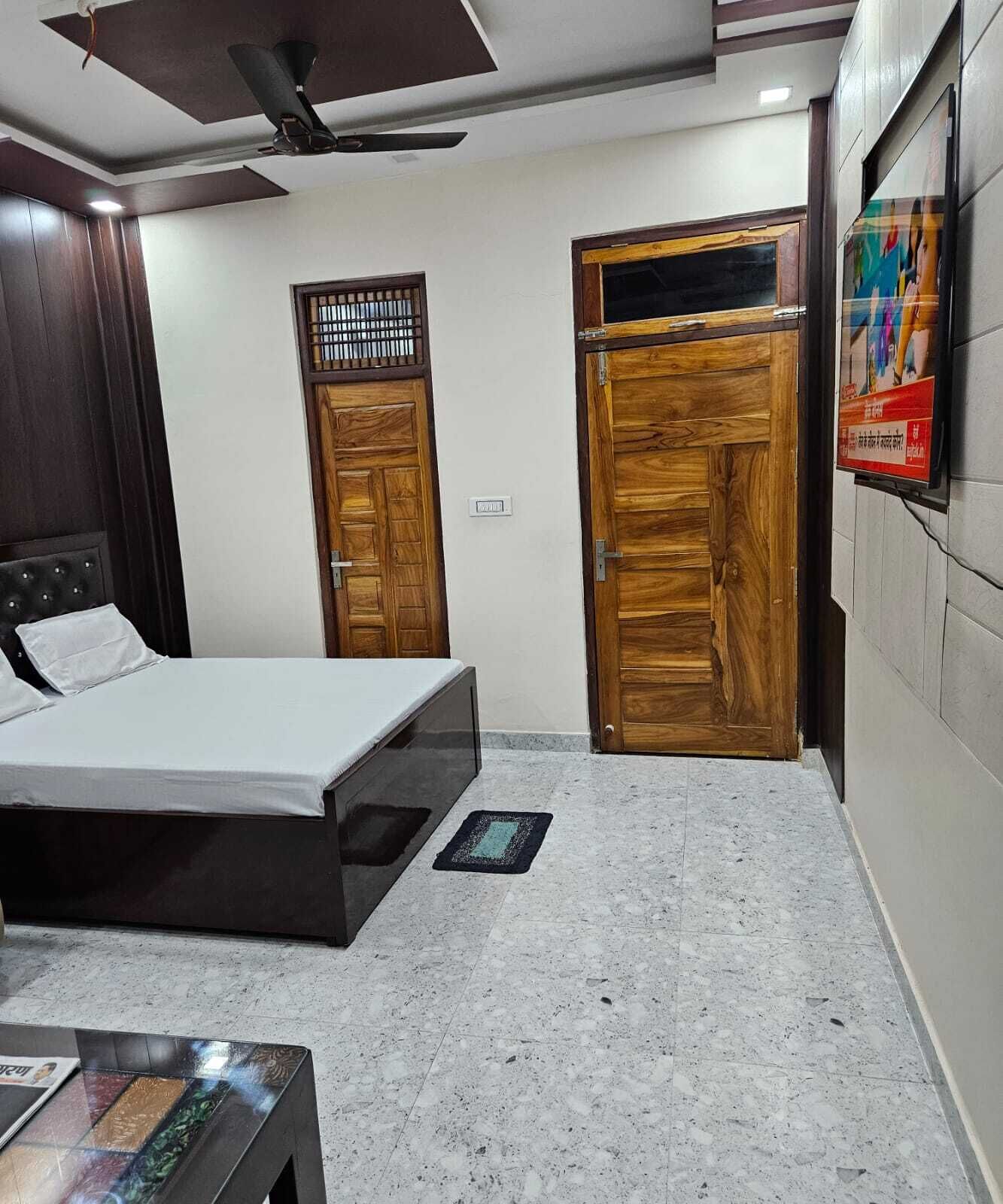 A bedroom with a bed, a ceiling fan, wooden doors, a tiled floor, and a small table.