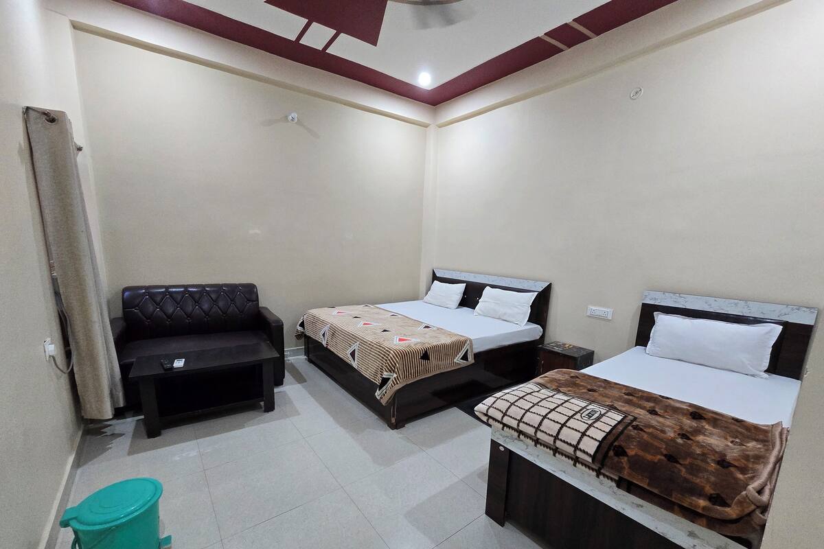 A room with two beds, a sofa, a small table, and a trash bin.