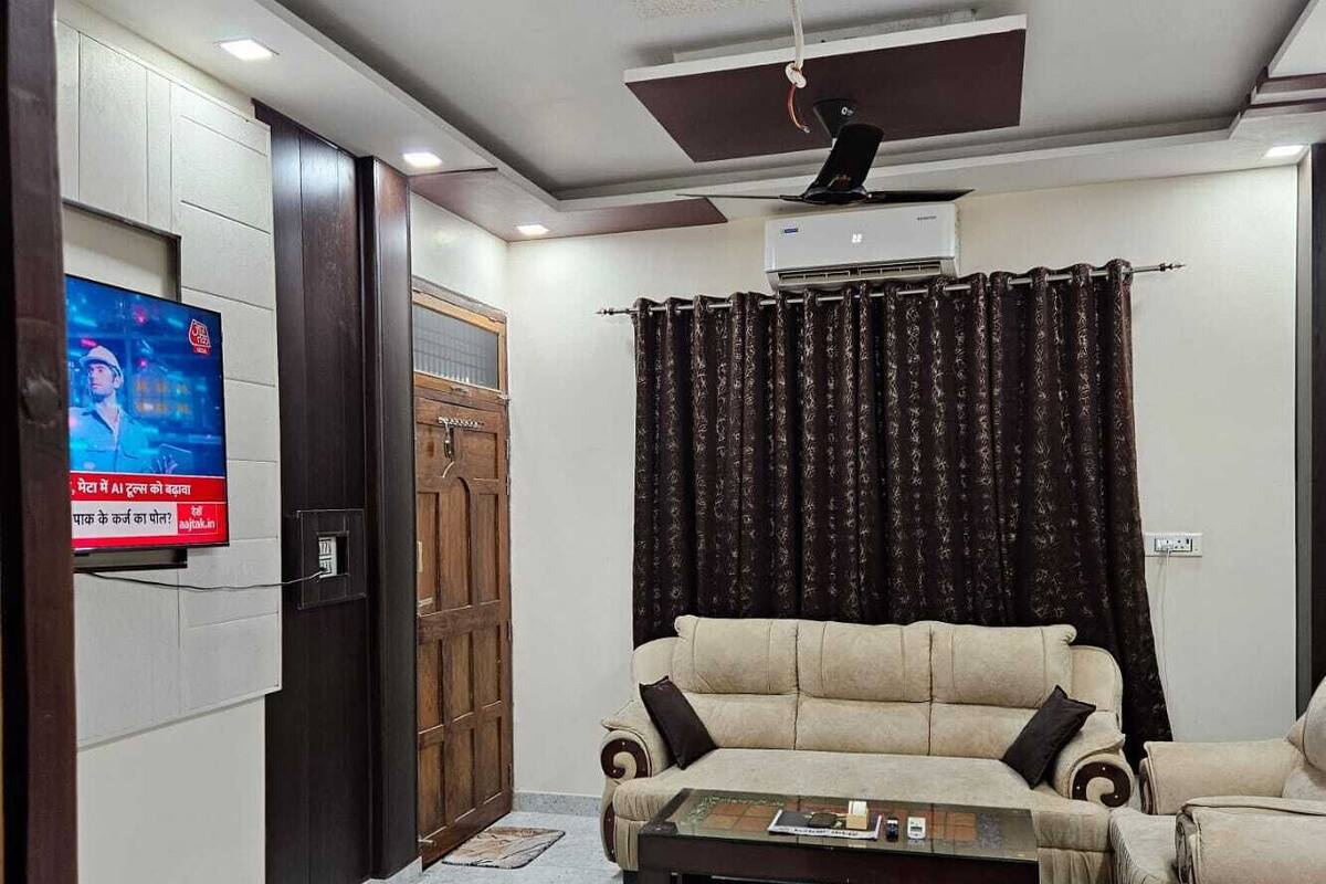 A living room with a sofa, a coffee table, a TV mounted on the wall, a ceiling fan, and an air conditioning unit.