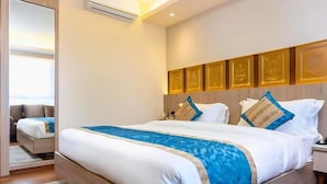 A hotel room with a large bed, a nightstand, a mirror, and a wall with framed artwork. - Hotel Siddhi Palace (Ayodhya)