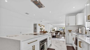 Una cocina moderna con armarios blancos, una isla central y un comedor al fondo.