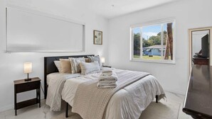 Un dormitorio con cama, mesitas de noche, ventana y vistas al exterior.