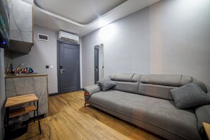 Ein kleiner Wohnbereich mit Sofa, einem Holztisch, einer Klimaanlage und einer Tür.