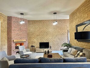 A living room with a brick fireplace, a flat-screen TV, and modern furniture. - Lake Villa 3 Bedrooms (Grombalia)