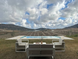 A pool with lounge chairs and a table, surrounded by a grassy area and hills in the background. - Lake Villa 3 Bedrooms (Grombalia)