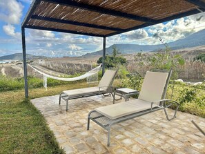 Zona relax all'aperto con due poltrone prendisole e un'amaca, con vista su un paesaggio montuoso.