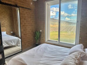 A bedroom with a large window, a bed, a bedside table, a mirror, and a potted plant. - Lake Villa 3 Bedrooms (Grombalia)