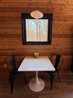 Une table avec deux chaises, un luminaire suspendu et une fenêtre donnant sur des arbres.