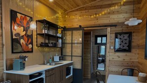 Une cuisine moderne avec des meubles en bois, un plan de travail blanc et un évier. On y trouve également un coin repas avec une table et des chaises, ainsi qu’un grand miroir accroché au mur.