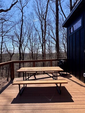 Une terrasse en bois avec une table de pique-nique, entourée d’arbres et d’un bâtiment.