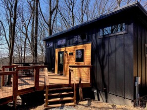 Eine Holzhütte mit einer Holzterrasse, schwarzem Anstrich und einem Fenster.