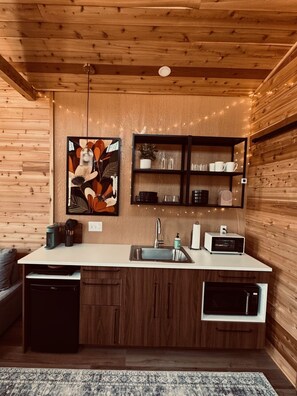 Une cuisine compacte avec des murs en bois, un plan de travail blanc, un évier, un four à micro-ondes et un petit réfrigérateur.