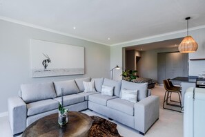 Una sala moderna con un sofá seccional gris, una mesa de centro redonda y una lámpara colgante.