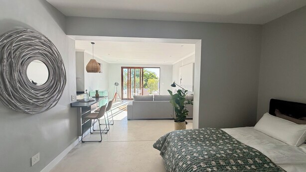 Camera moderna con un letto, un grande specchio e vista sul soggiorno.