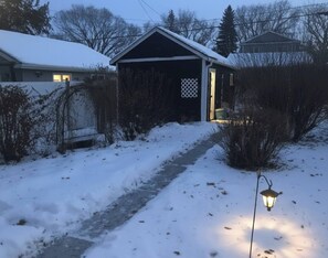 En snedækket sti, der fører hen til et hus med garage, omgivet af vegetation.