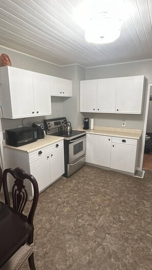A compact kitchen with white cabinets, a microwave, an oven, and a kettle. - Quiet Heritage Bungalow Entire Home Geodome (Edmonton)