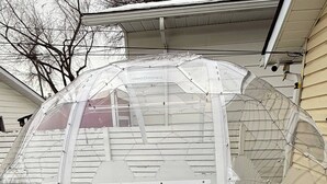 A transparent geodesic dome structure with a green artificial turf base, attached to a building. - Quiet Heritage Bungalow Entire Home Geodome (Edmonton)