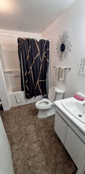 Et badeværelse med bruseforhæng, toilet, vask og et håndklædestativ på væggen.