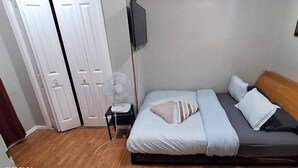 A bedroom with a bed, bedside table, fan, and a TV mounted on the wall. - Quiet Heritage Bungalow Entire Home Geodome (Edmonton)