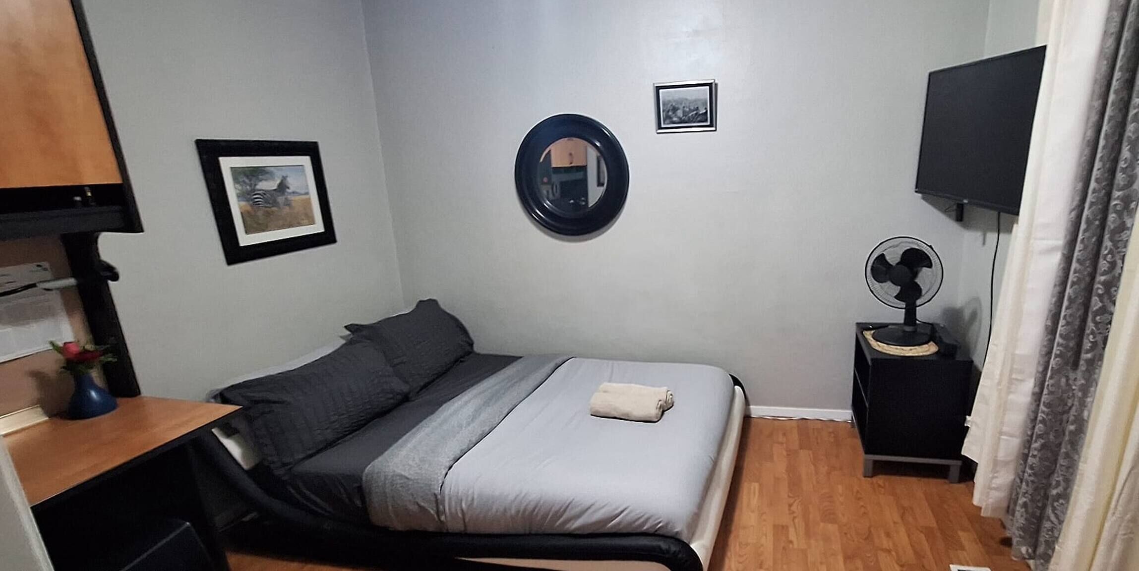 Une chambre à coucher avec un lit, un bureau, un miroir, un ventilateur et une télévision.