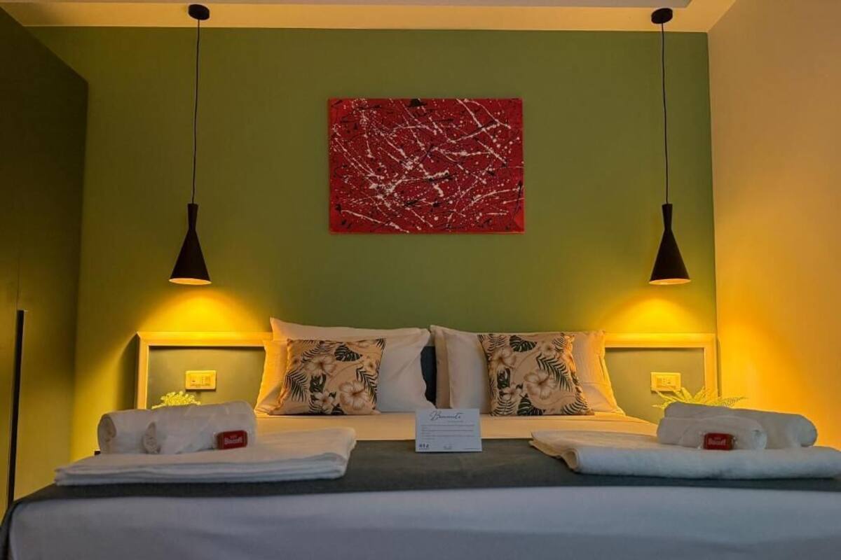 A hotel room with a bed, two bedside lamps, a red abstract painting on the wall, and a sign on the bed.
