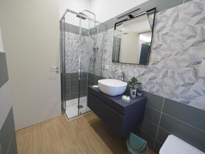 A modern bathroom with a glass shower enclosure, a large white sink, a dark vanity, and a mirror above the sink.