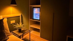 A cozy room with a sofa, a small table with a plant, a TV on a shelf, and a hanging light fixture. - Casa Teresa Guest Rooms (Parghelia)