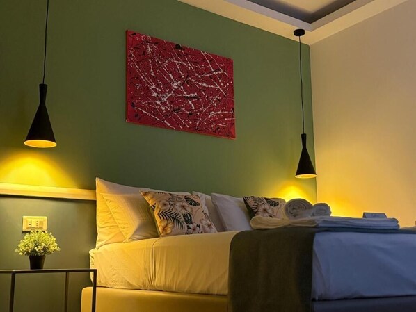 A hotel room with a bed, two pendant lights, a red abstract painting, and a small potted plant.