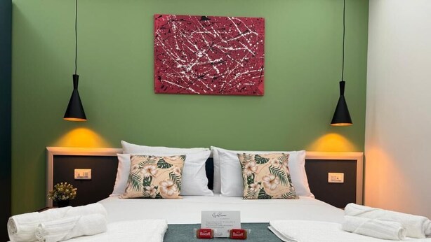 A hotel room with a bed, two bedside lamps, a red abstract painting, floral pillows, and neatly folded towels. - Casa Teresa Guest Rooms (Parghelia)