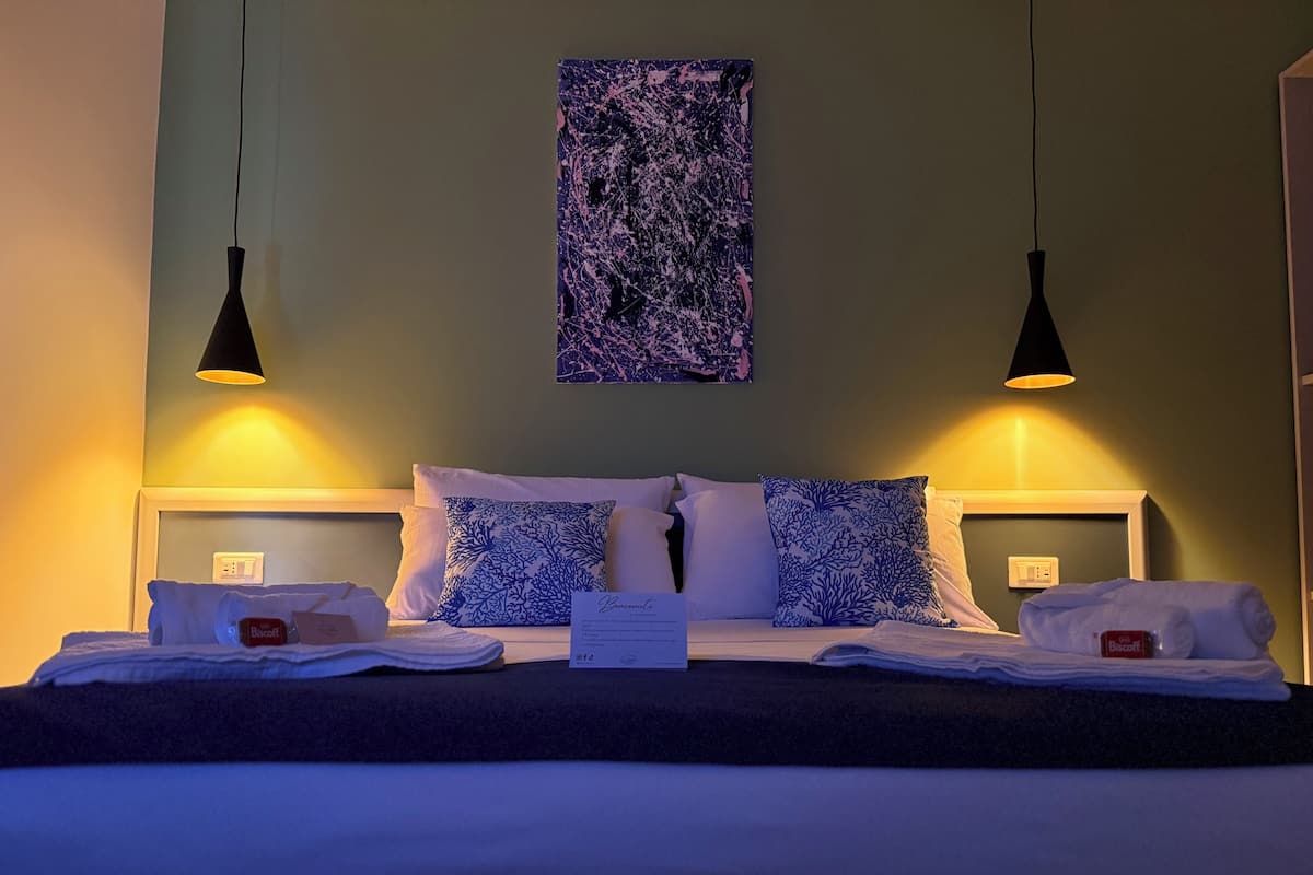 A neatly made bed with a pillow, a bedside table with a tissue box, and a wall-mounted painting.