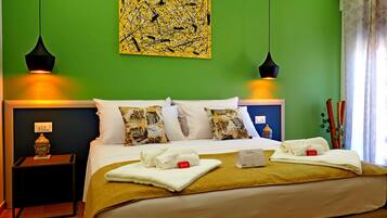 A neatly made bed with a green wall, two black pendant lights, and a Buddha statue on a nightstand.