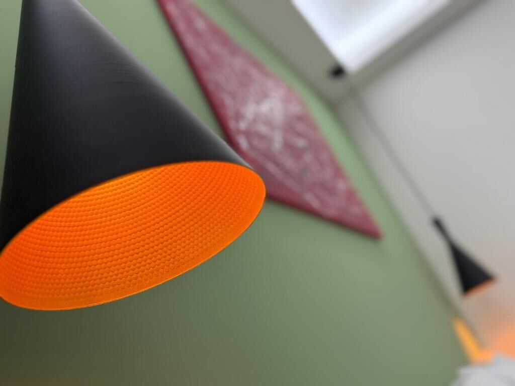 A close-up of a black and orange cone-shaped object, possibly a decorative item, against a green wall with a red patterned object in the background.