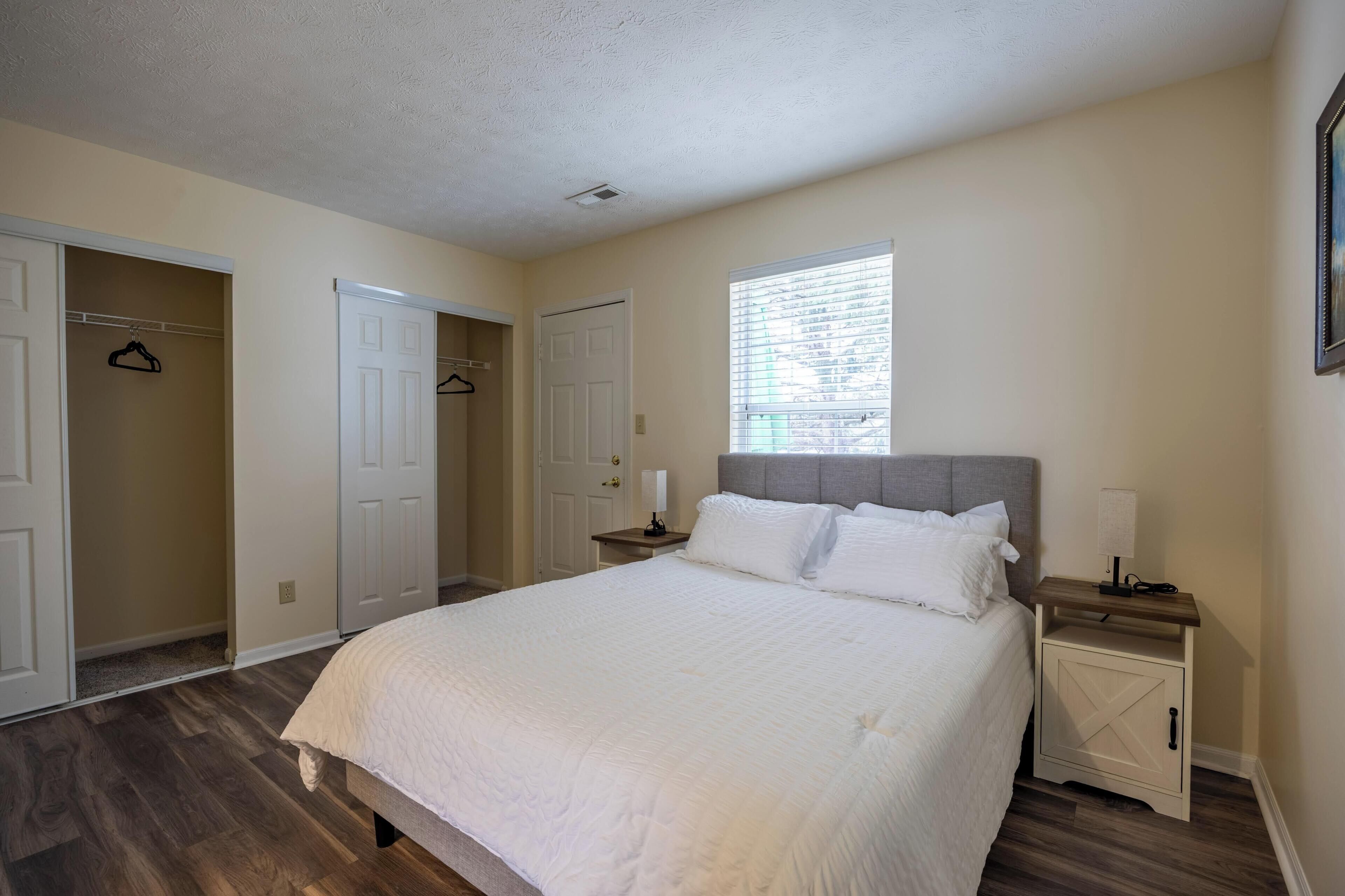 A bedroom with a bed, a nightstand, a window, and a closet.