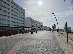 A coastal hotel with multiple floors, a paved walkway, and a clear sky. - 3BR Beachfront · Direct Sea View · Covered Terrace · Prime Location · A/C · WiFi (Quarteira)