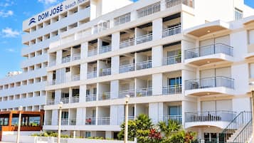 Um hotel de vários andares com varandas, uma placa com a inscrição 'DOM JOSÉ beach hotel' e uma área pavimentada na frente.