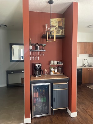 Une cuisine compacte équipée d’une machine à café, de verres à vin et d’un mini-réfrigérateur.