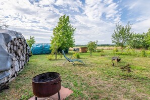 A rural outdoor area with a metal barrel, a covered stack of logs, a blue tarp, a chair, and a wheelbarrow. - Holiday Apartment - Neu Dessau (Milower Land)