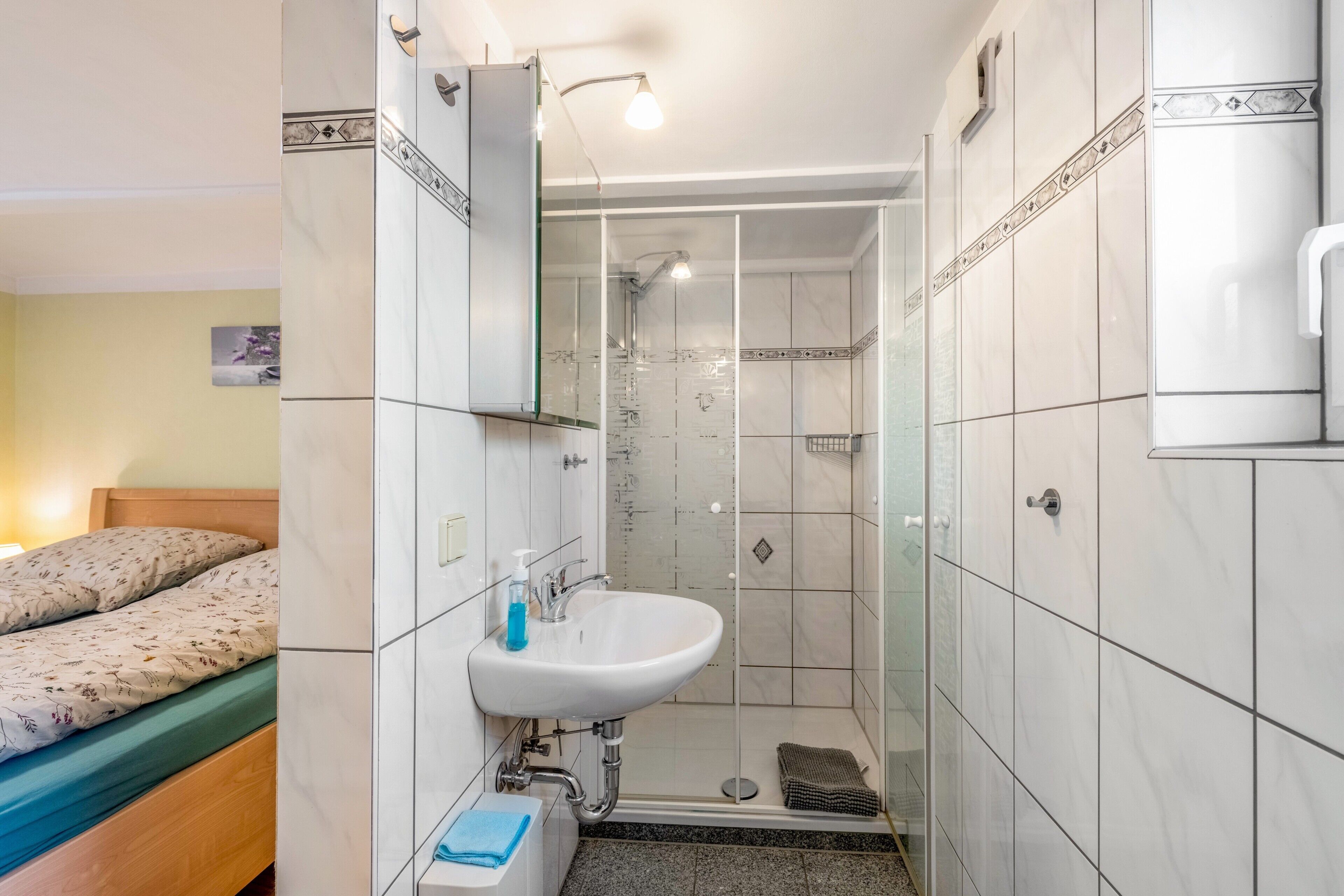 Et badeværelse med bruser, vask og toilet, med hvide fliser og en træseng.