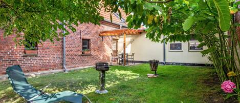 A backyard with a brick house, a wooden pergola, a fire pit, and a green lawn.