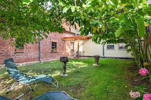 A backyard with a brick house, a wooden pergola, a fire pit, and a green lawn.