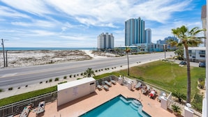 A hotel with a pool, lounge chairs, and a view of the beach and city skyline. - Grand Beach Resort 310 (Gulf Shores)