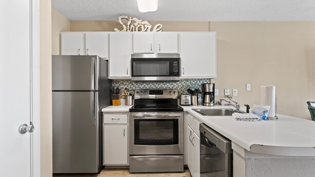 A modern kitchen with stainless steel appliances, white cabinets, and a tiled backsplash. - Grand Beach Resort 310 (Gulf Shores)