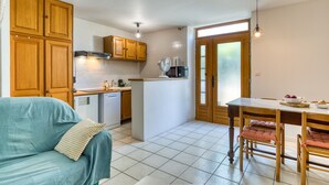 A kitchen with wooden cabinets, a dining table with chairs, a sofa, and a refrigerator.