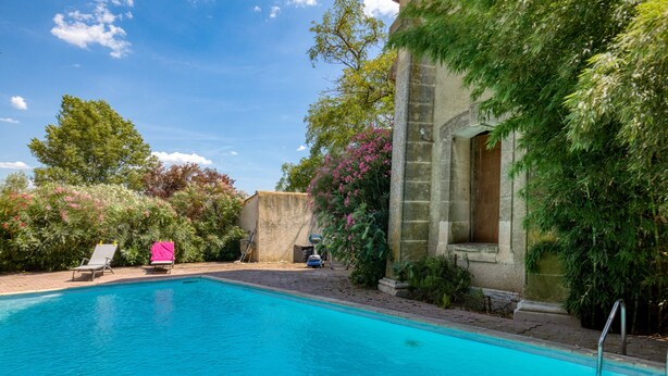 A swimming pool with lounge chairs, a stone building, and lush greenery.