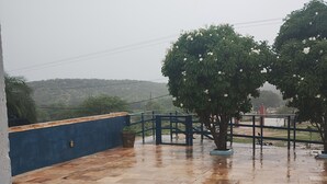 A wet patio with a railing, a tree, and a view of a hilly landscape. - Hotel fazenda serrota t (Currais Novos)