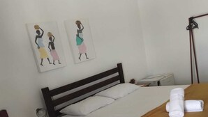 A hotel room with two single beds, a bedside table with a lamp, a wall-mounted heater, and two artwork pieces depicting women. - Hotel fazenda serrota t (Currais Novos)