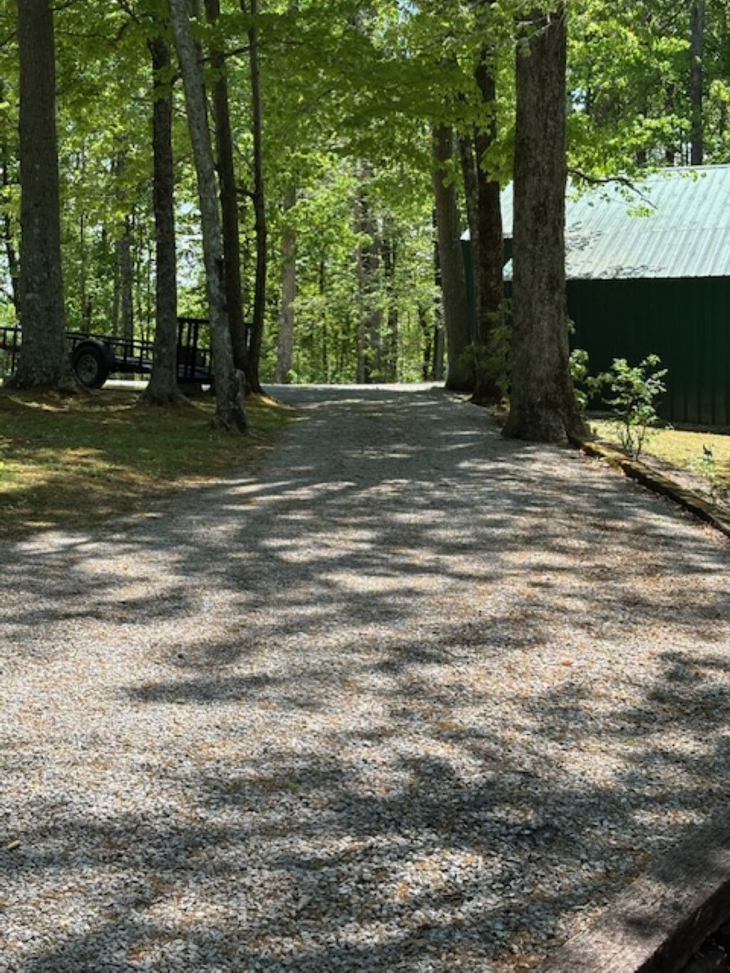 A gravel path leading through a wooded area with trees on both sides and a green building in the distance.